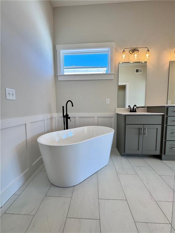 bathroom featuring vanity, a freestanding tub, a decorative wall, and a wainscoted wall