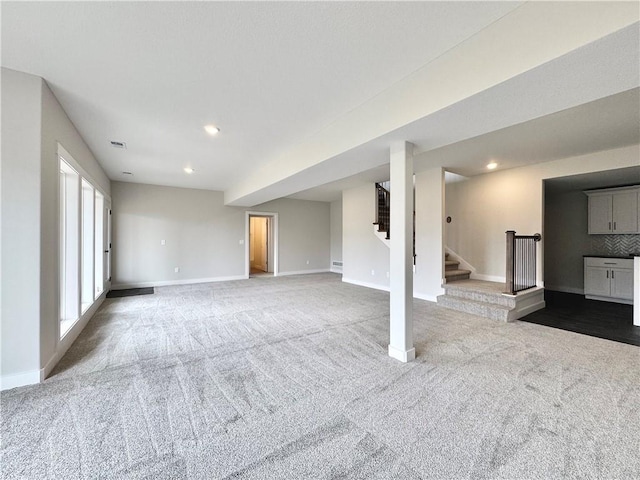 unfurnished living room with baseboards, carpet, and stairs