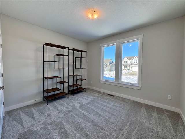 unfurnished room with carpet flooring, visible vents, baseboards, and a textured ceiling