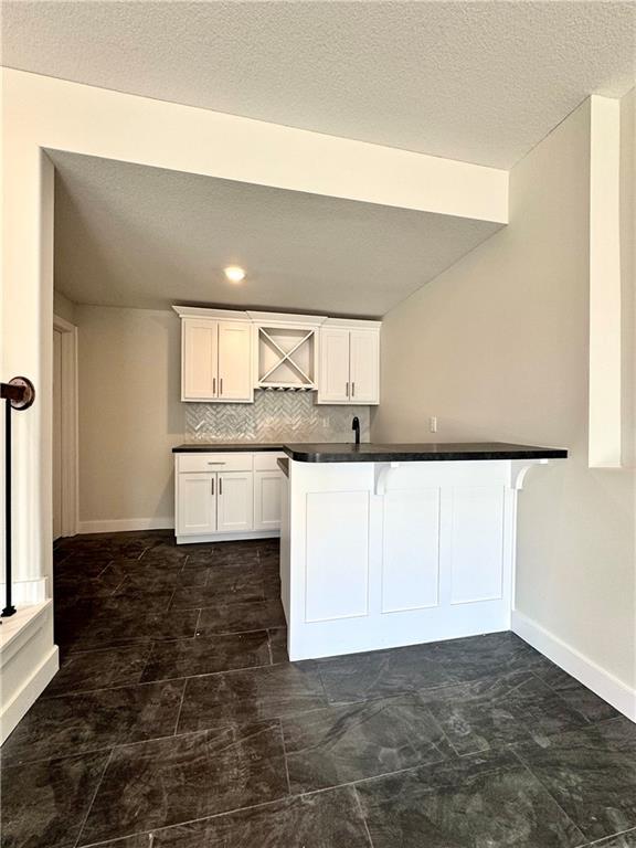 kitchen with dark countertops, decorative backsplash, white cabinets, and baseboards