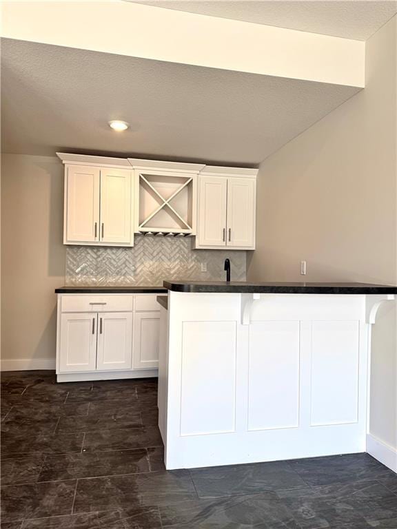 kitchen featuring backsplash, baseboards, dark countertops, and white cabinets