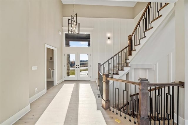 foyer entrance with french doors, a towering ceiling, light hardwood / wood-style flooring, and a notable chandelier