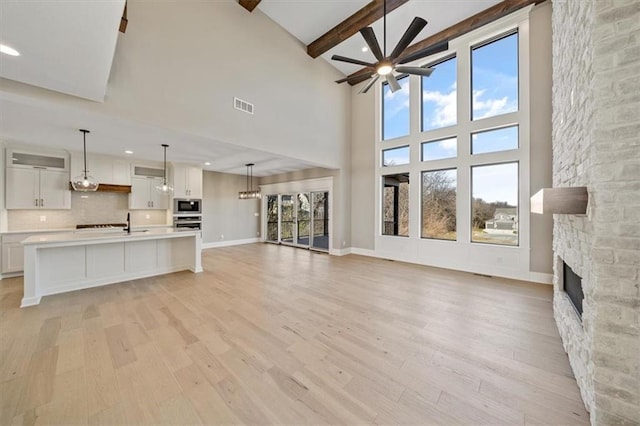 unfurnished living room with light wood-type flooring, a fireplace, a wealth of natural light, and a towering ceiling