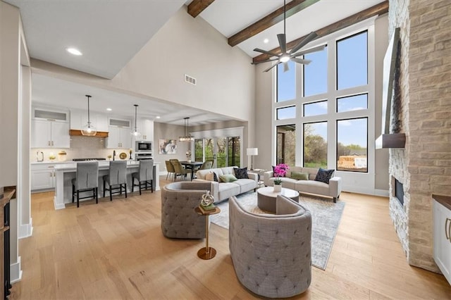 living room featuring baseboards, beam ceiling, ceiling fan, light wood-style flooring, and a fireplace