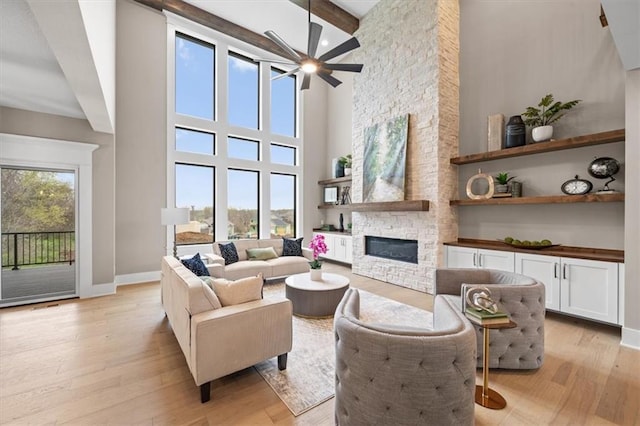 living area with light wood-style flooring, a stone fireplace, a healthy amount of sunlight, and ceiling fan