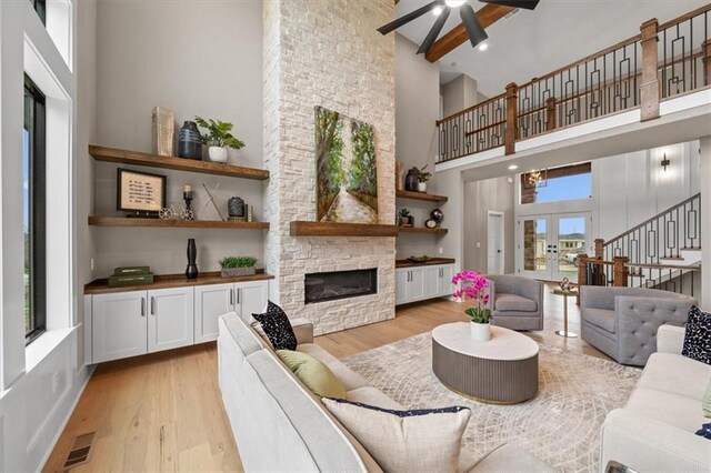 living area featuring a towering ceiling, light wood-style floors, a fireplace, and ceiling fan