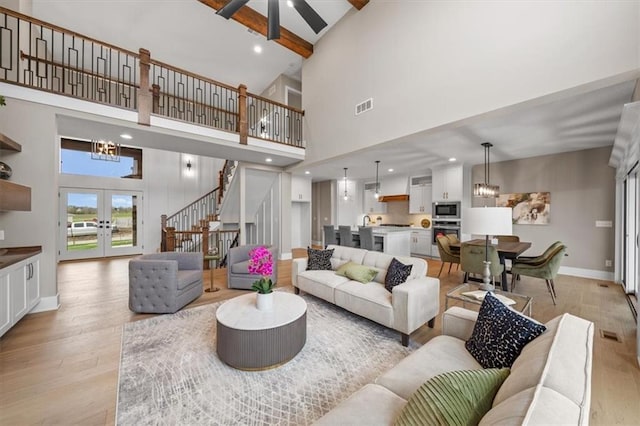 living room featuring stairway, light wood-type flooring, visible vents, baseboards, and beamed ceiling