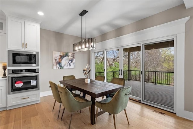 dining room with baseboards, light wood-type flooring, visible vents, and an inviting chandelier