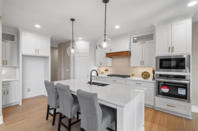 kitchen featuring premium range hood, stainless steel appliances, a sink, light wood finished floors, and white cabinets