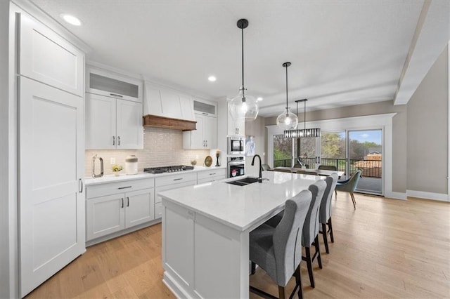 kitchen featuring tasteful backsplash, stainless steel appliances, a sink, light wood finished floors, and white cabinets