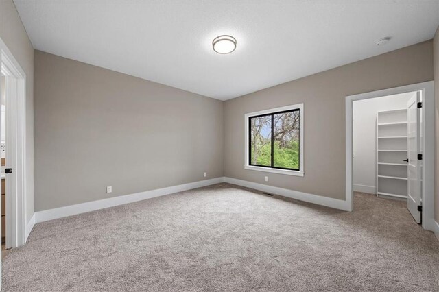 unfurnished bedroom with carpet floors, a walk in closet, baseboards, and a closet