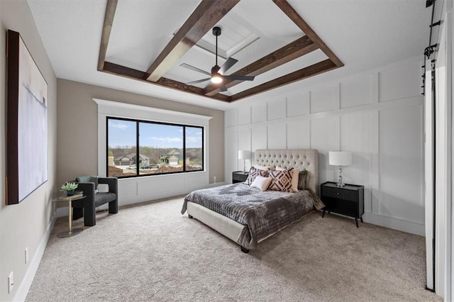 carpeted bedroom featuring a barn door, a decorative wall, ceiling fan, and beamed ceiling