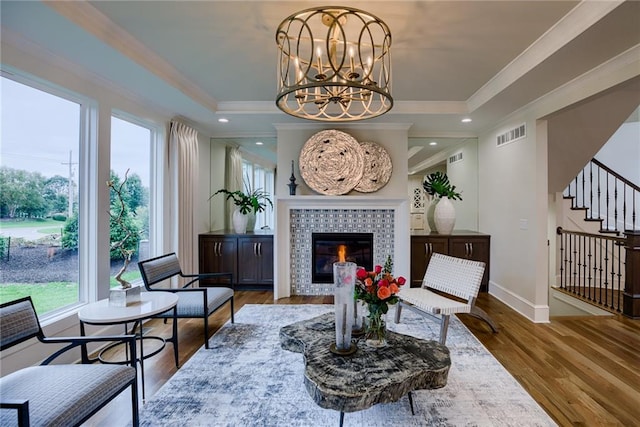 living room with wood-type flooring, a fireplace, a notable chandelier, and crown molding