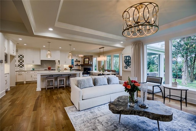 living room with a chandelier, ornamental molding, wood-type flooring, and a raised ceiling