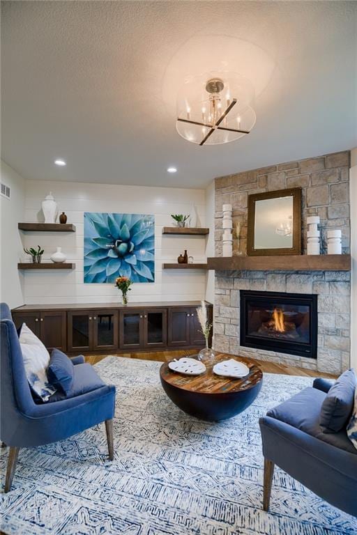 living room featuring a textured ceiling, a chandelier, and a stone fireplace