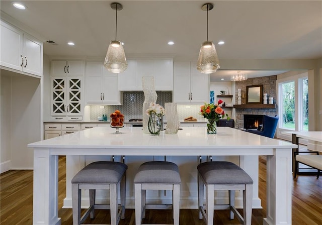 kitchen with wood-type flooring, hanging light fixtures, white cabinetry, and a fireplace