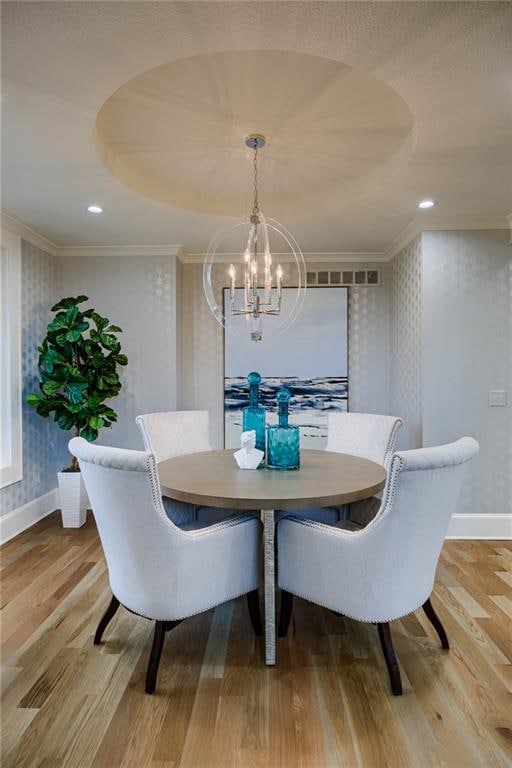 dining space with ornamental molding, an inviting chandelier, and light hardwood / wood-style flooring