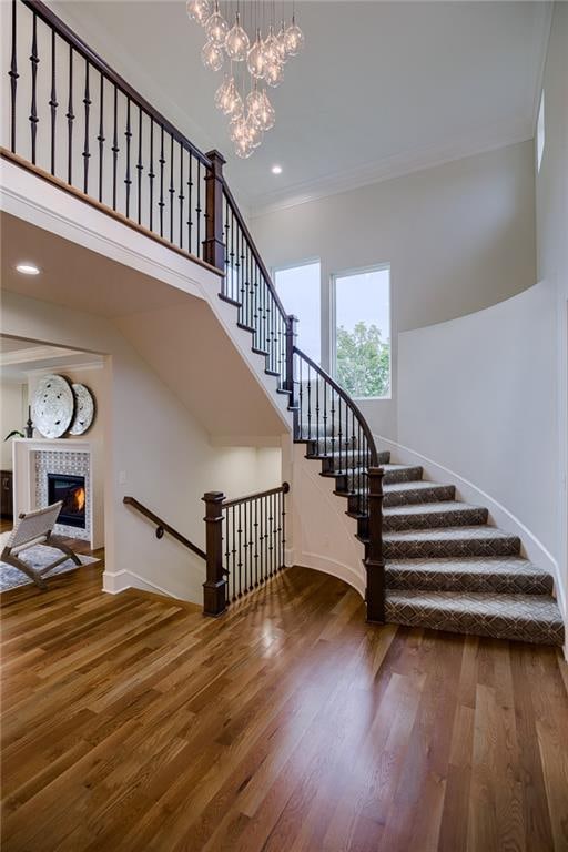 staircase featuring an inviting chandelier, a tile fireplace, hardwood / wood-style flooring, and crown molding