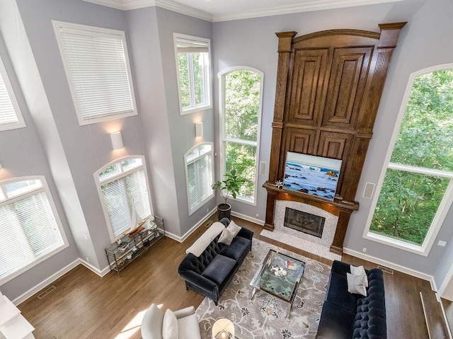 living room with a tile fireplace, ornamental molding, hardwood / wood-style floors, and a towering ceiling