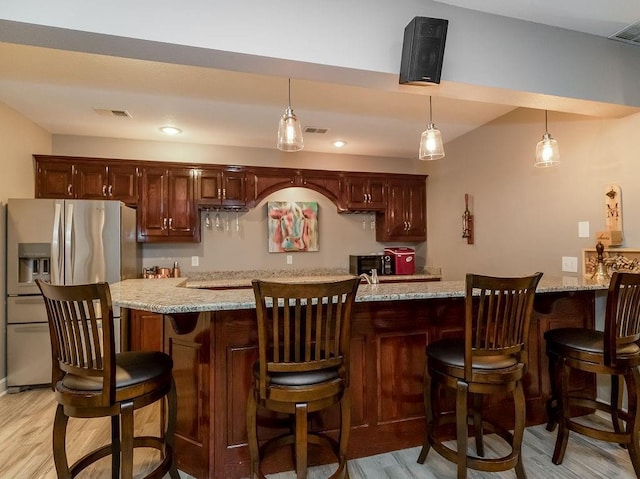 interior space featuring stainless steel fridge with ice dispenser, light stone countertops, hanging light fixtures, and light wood-type flooring