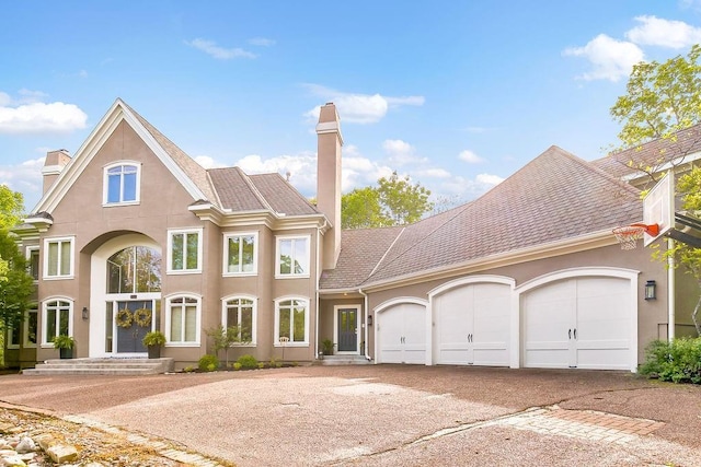 view of front facade featuring driveway, a chimney, and stucco siding