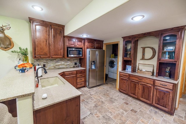 kitchen with light tile flooring, backsplash, stainless steel appliances, sink, and washer / dryer