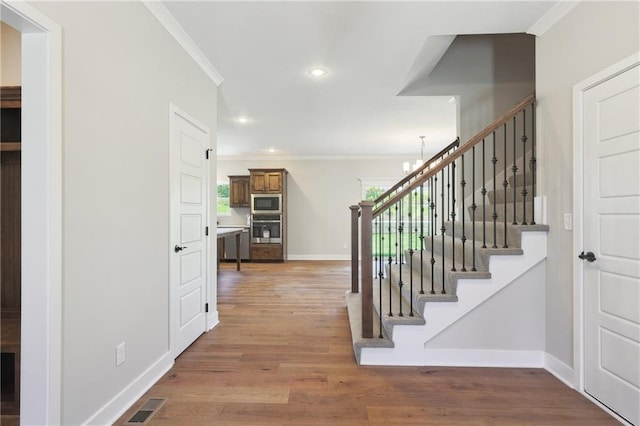 stairs with ornamental molding, a wealth of natural light, visible vents, and wood finished floors