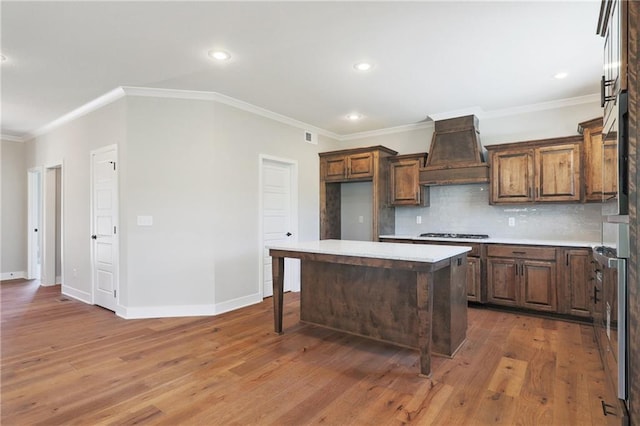 kitchen featuring custom range hood, decorative backsplash, crown molding, a kitchen island, and hardwood / wood-style flooring