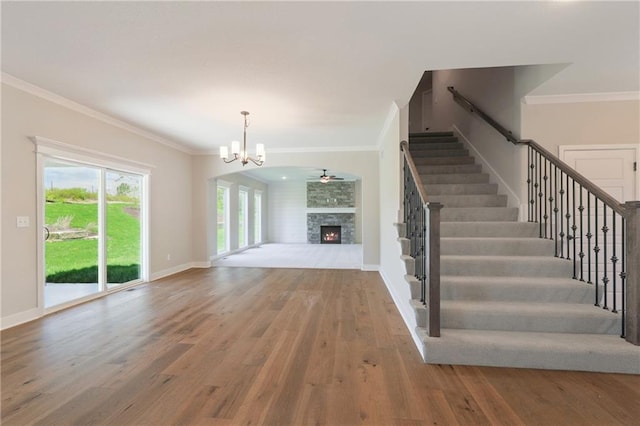 unfurnished living room with hardwood / wood-style flooring, crown molding, a chandelier, and a stone fireplace