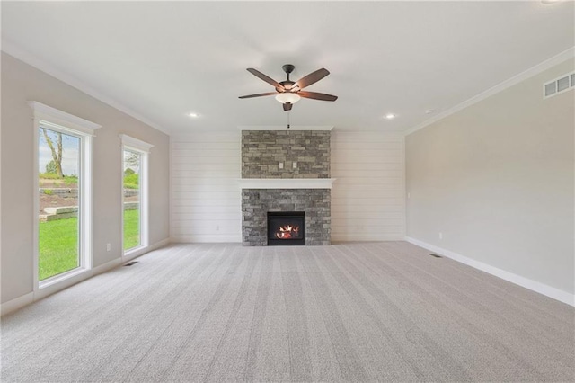 unfurnished living room featuring ceiling fan, crown molding, a stone fireplace, and light carpet