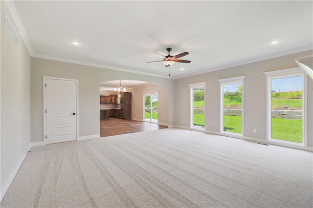 unfurnished living room featuring light colored carpet, ornamental molding, ceiling fan, and a wealth of natural light