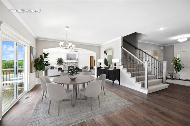 dining area featuring crown molding, a lit fireplace, stairway, dark wood-style floors, and an inviting chandelier