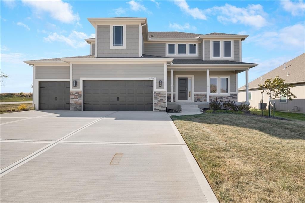 prairie-style house featuring stone siding, a front yard, covered porch, and an attached garage