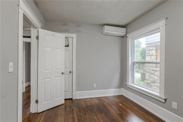 unfurnished bedroom featuring a textured ceiling, dark wood-type flooring, multiple windows, and a wall mounted air conditioner