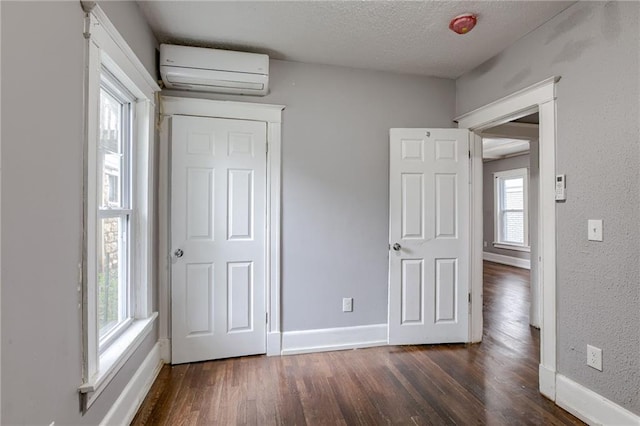 unfurnished bedroom featuring a textured ceiling, a wall mounted air conditioner, multiple windows, and dark hardwood / wood-style flooring