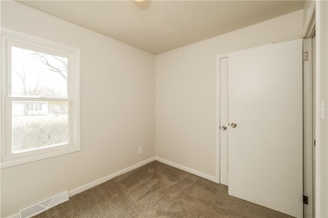 unfurnished room with plenty of natural light and dark carpet