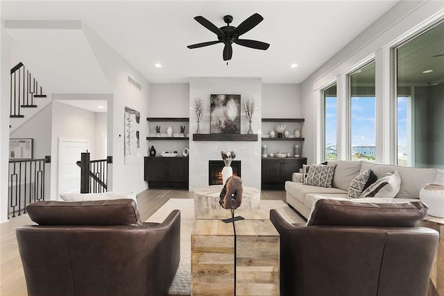 living room with a fireplace, light wood-type flooring, and ceiling fan