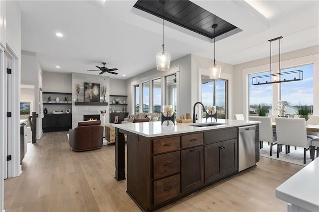 kitchen with stainless steel dishwasher, sink, decorative light fixtures, a fireplace, and an island with sink