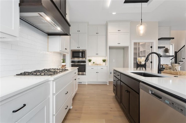 kitchen featuring sink, stainless steel appliances, wall chimney range hood, decorative light fixtures, and white cabinets