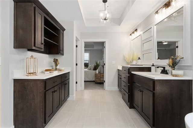 bathroom with tile patterned flooring, vanity, ceiling fan with notable chandelier, and a raised ceiling