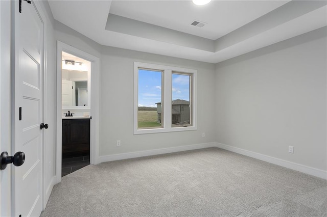 unfurnished bedroom with carpet, sink, a tray ceiling, and ensuite bath