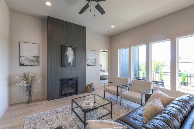 living room with ceiling fan, light hardwood / wood-style flooring, a large fireplace, and a wealth of natural light