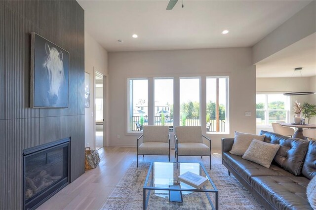 living room featuring light wood-type flooring, ceiling fan, and a large fireplace