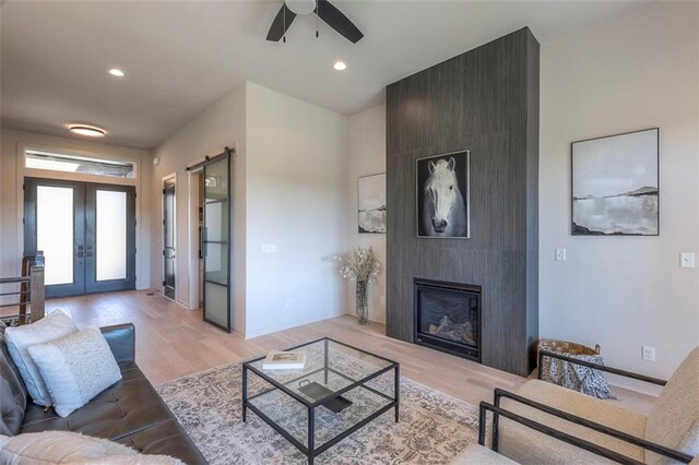 living room featuring french doors, a fireplace, light hardwood / wood-style floors, and ceiling fan