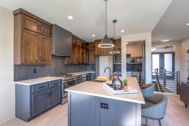 kitchen featuring a kitchen island with sink, light wood-type flooring, sink, and stainless steel range oven