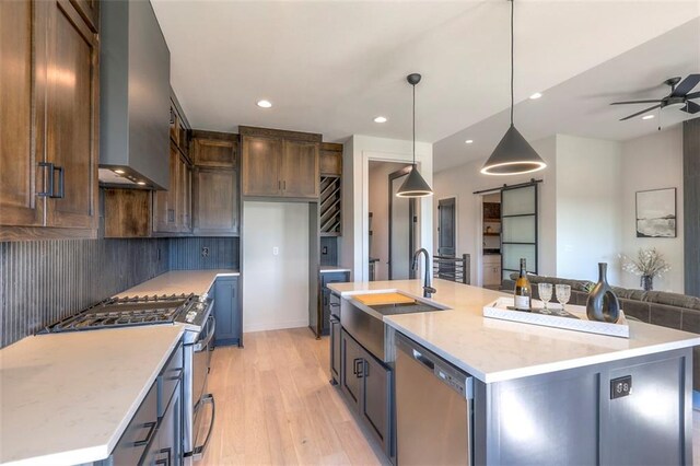 kitchen featuring ceiling fan, decorative light fixtures, a large island with sink, light hardwood / wood-style flooring, and stainless steel appliances