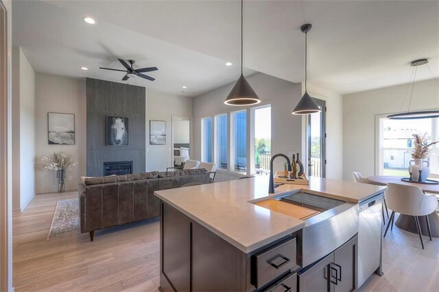 kitchen with a large fireplace, pendant lighting, an island with sink, and ceiling fan