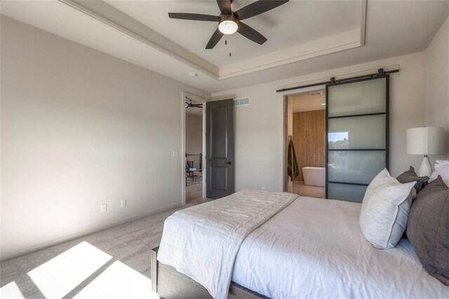 carpeted bedroom with ceiling fan, a raised ceiling, connected bathroom, and a barn door