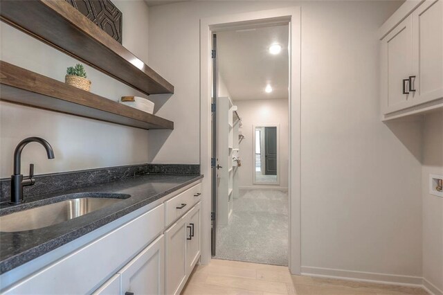 kitchen featuring dark stone countertops, white cabinets, light hardwood / wood-style flooring, and sink