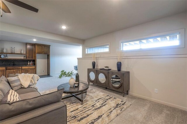 living room featuring ceiling fan, light colored carpet, sink, and a healthy amount of sunlight